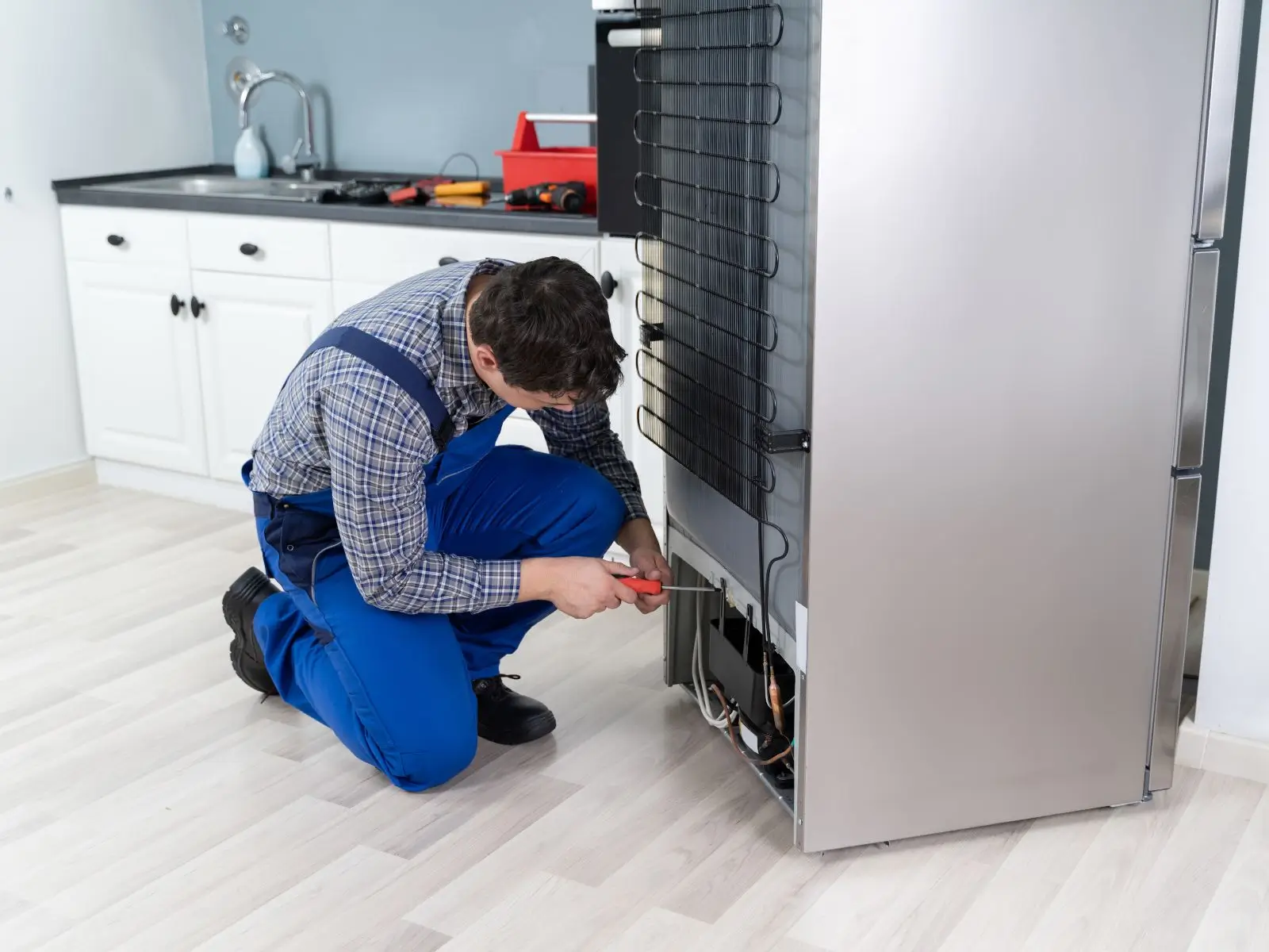 Appliance technician inspecting and repairing the back of a refrigerator in a residential kitchen