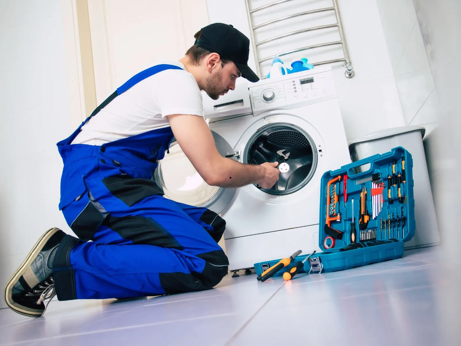Appliance technician repairing a front-load washing machine in a residential laundry room